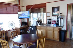 A small cafe with a wooden counter, a TV mounted on the wall, a fan, and a trash bin.