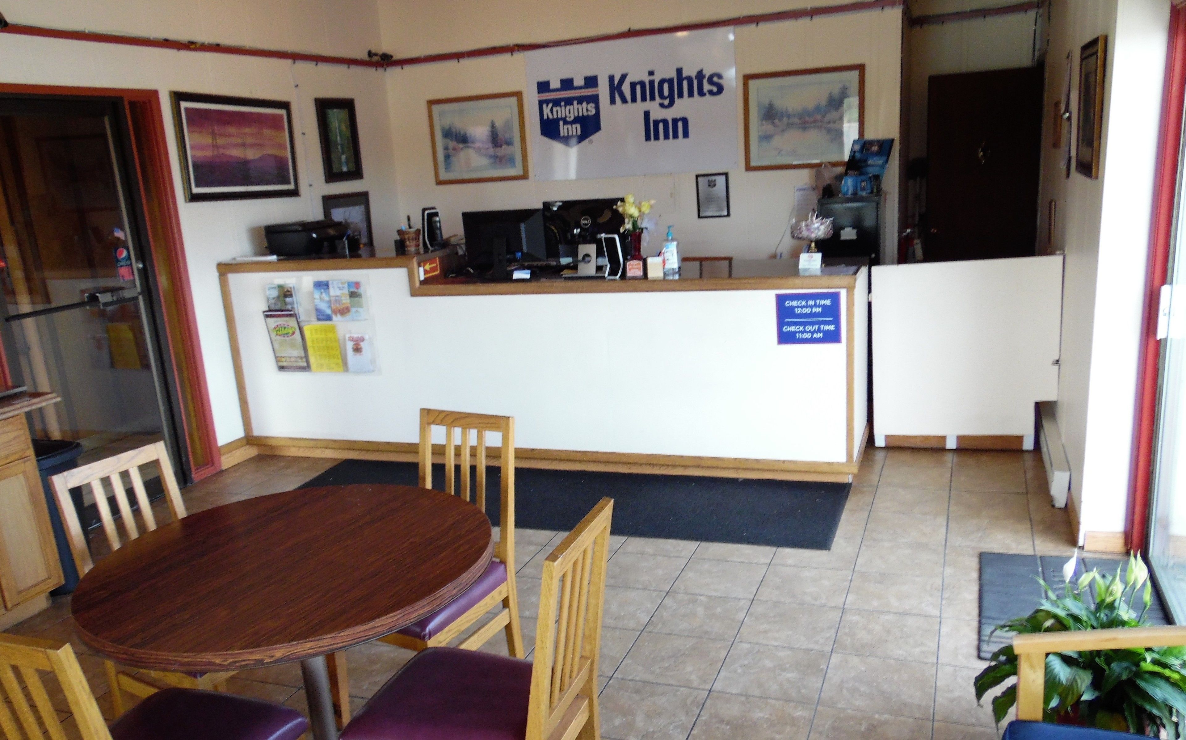 A Knights Inn reception area with a wooden reception desk, a check-in/out sign, and a dining area with a wooden table and chairs.