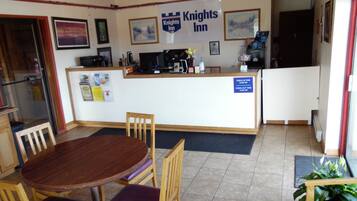 A Knights Inn reception area with a wooden reception desk, a check-in/out sign, and a dining area with a wooden table and chairs.