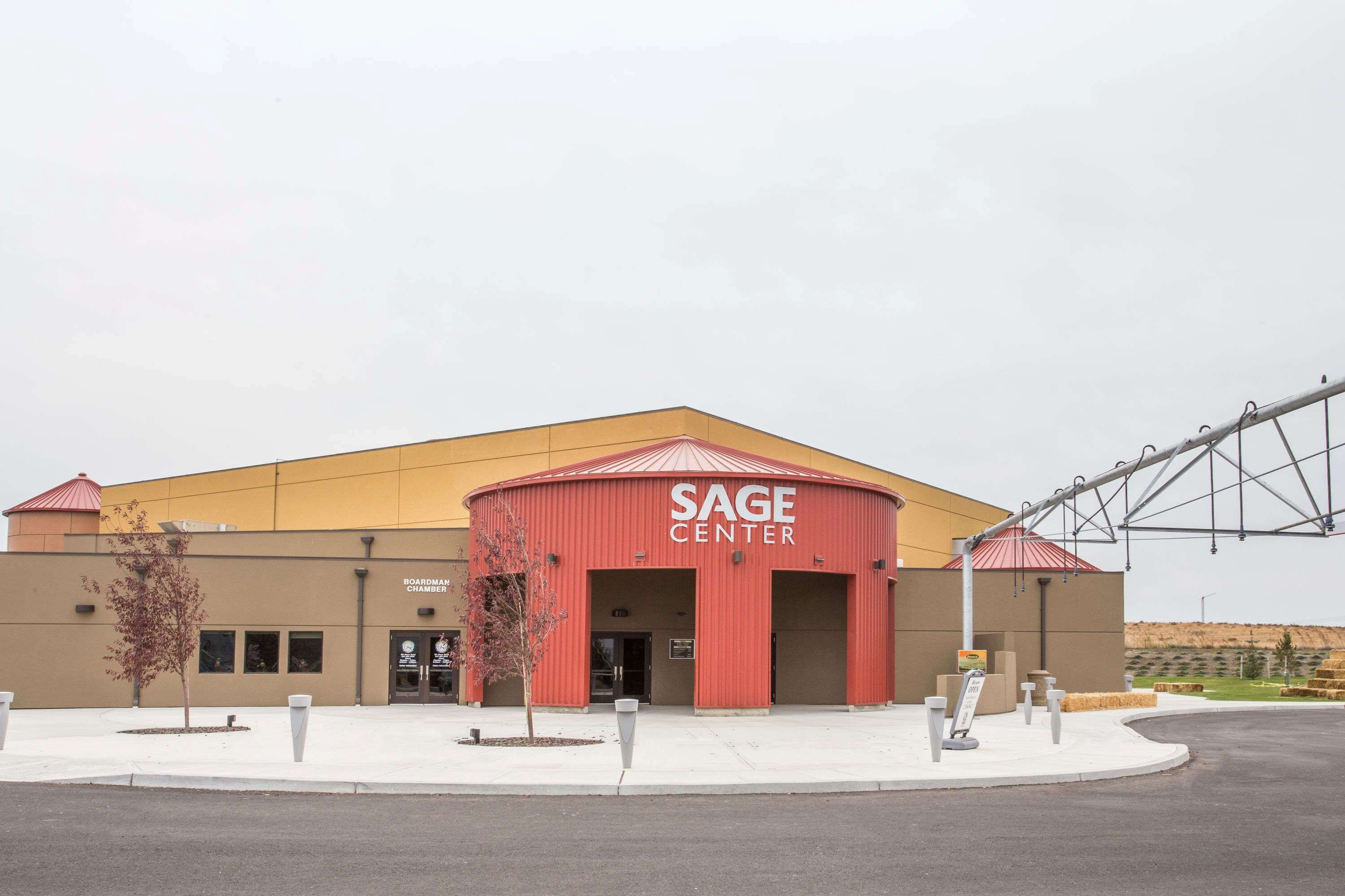 A building with a red and yellow exterior, labeled "SAGE CENTER," featuring a large entrance and a covered area with a red roof.
