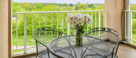 Ein runder Metalltisch mit einer Vase weißer Blumen auf einem Balkon mit weißer Brüstung.