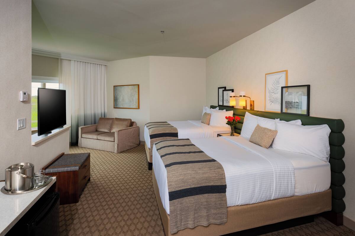 A hotel room with two beds, a television, a desk with a tray of items, and a chair.