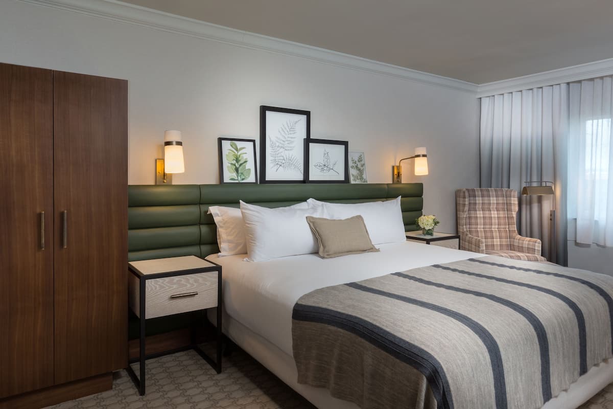 A hotel room with a large bed, a wooden wardrobe, a nightstand, and a chair.