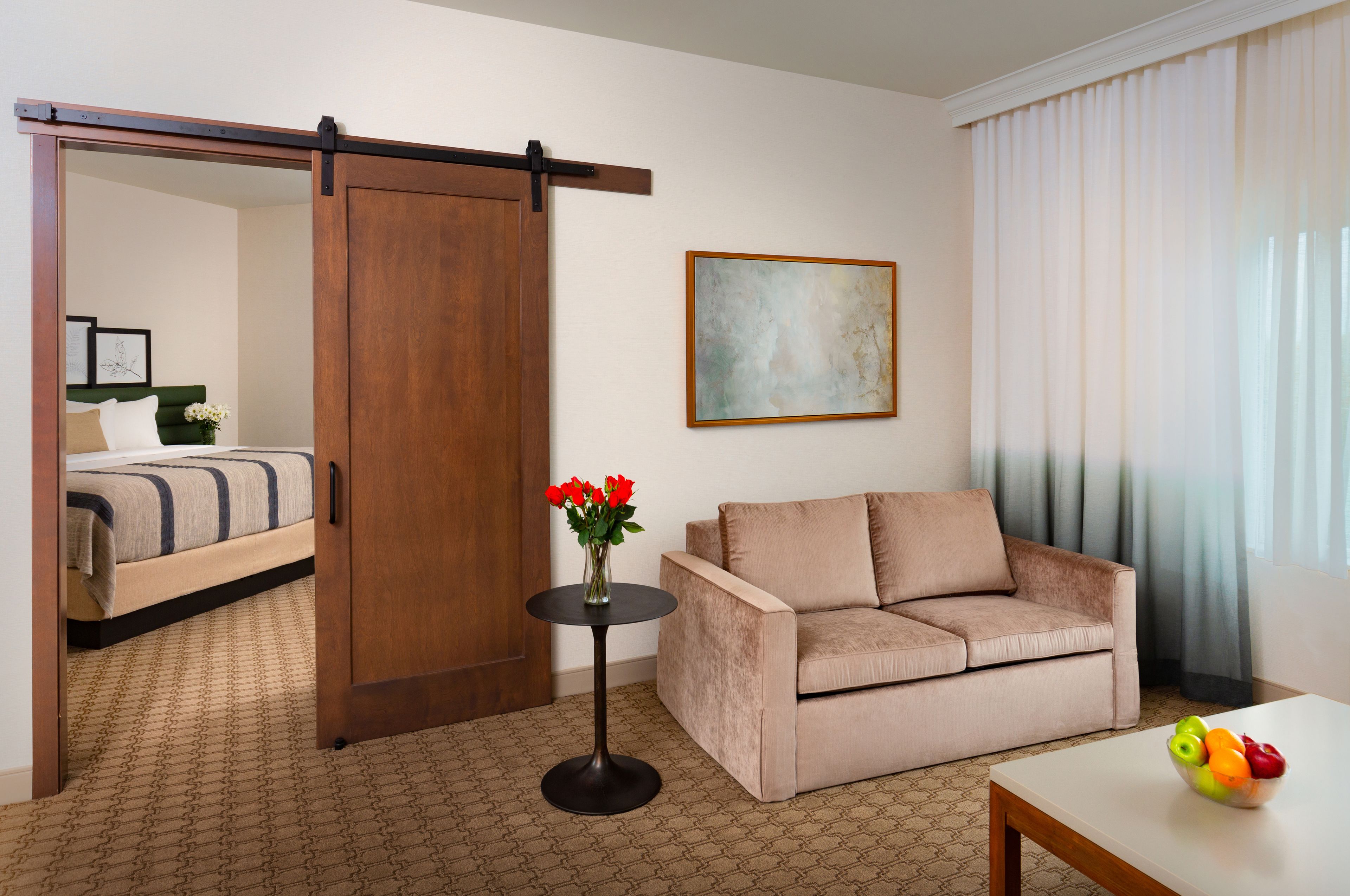 Ein Hotelzimmer mit einer Schiebetür, einem Sofa, einem kleinen Tisch mit Obstschale und einem Gemälde an der Wand.