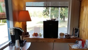 A compact kitchen with a window, a coffee machine, a refrigerator, and a wooden cabinet.