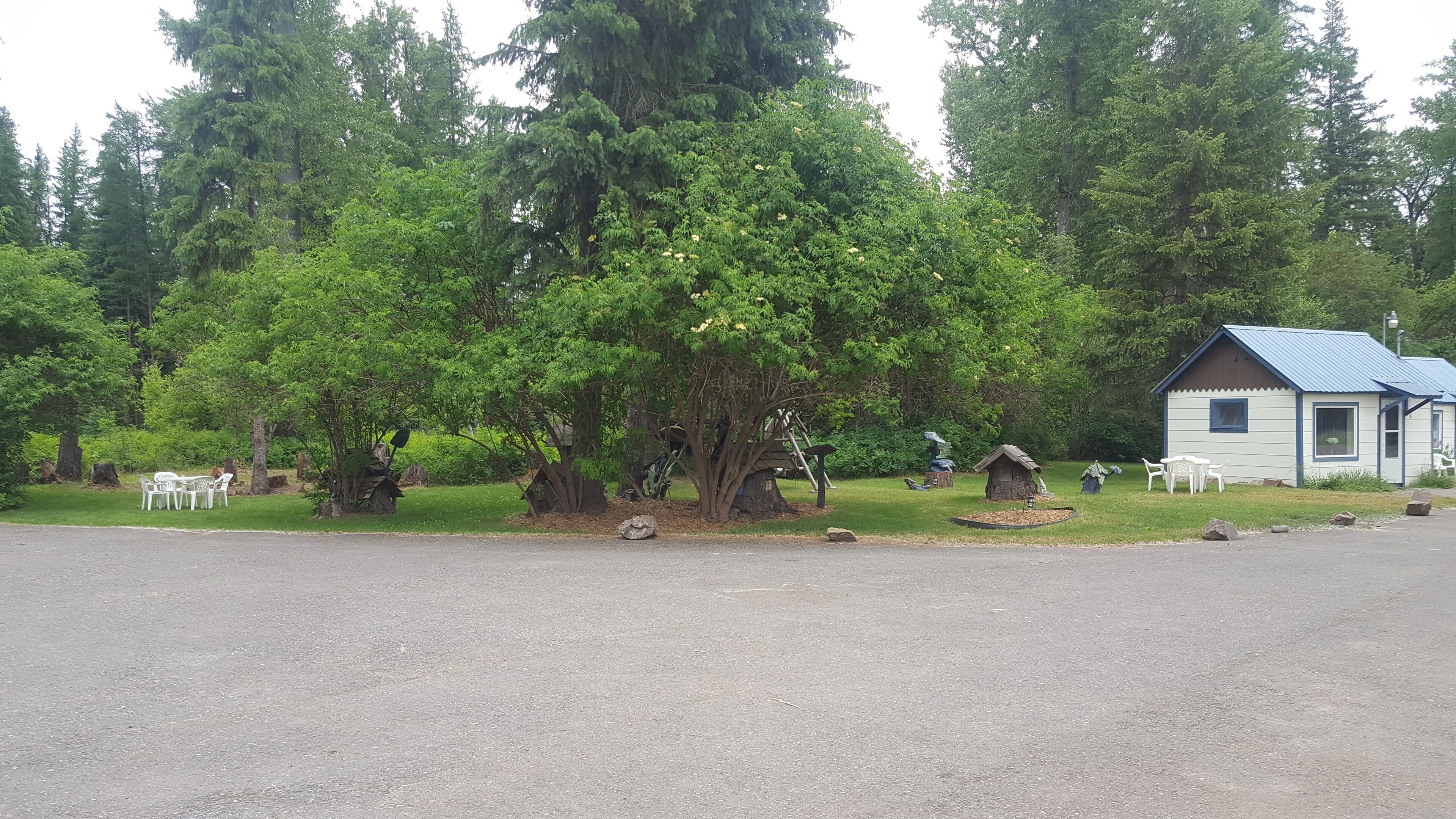 Un parque con mesas de picnic, una cabaña pequeña y varios árboles.