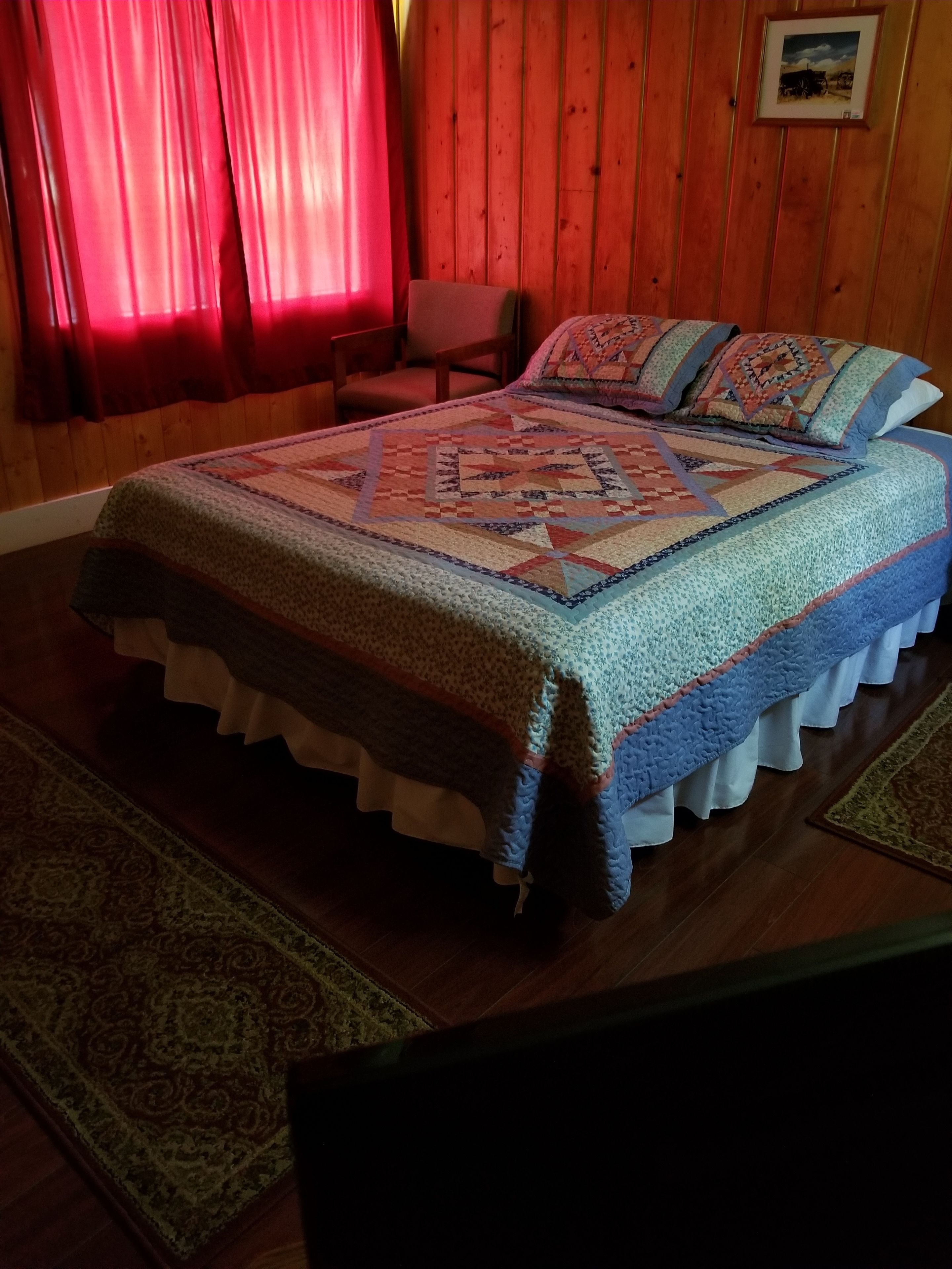 A bedroom with a large bed, a wooden headboard, a red chair, and a framed picture on the wall.