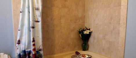 Une salle de bain avec une baignoire aux courbes élégantes, un rideau de douche orné de motifs marins, un vase rempli de fleurs et une serviette posée sur le bord de la baignoire.
