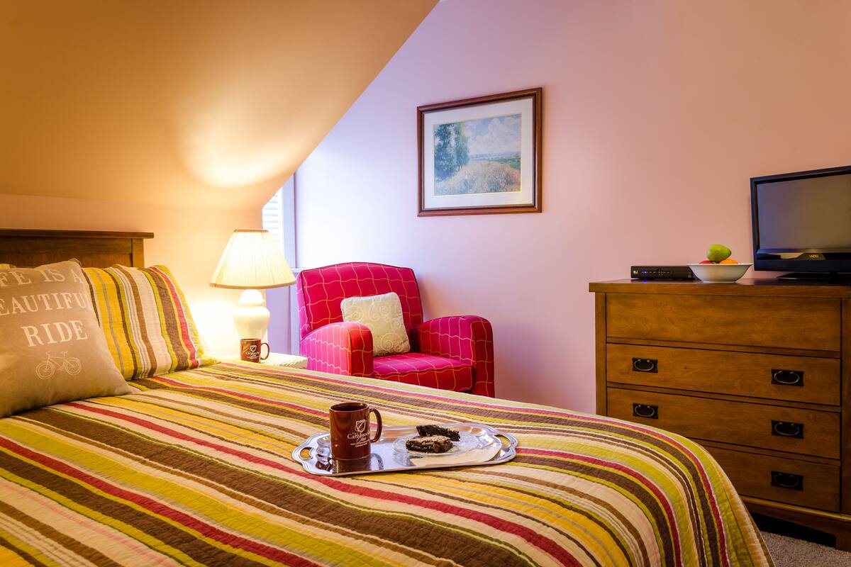 Ein Hotelzimmer mit einem Bett, einem roten Sessel, einem Holzschrank, einem Fernseher und einem Bild an der Wand.