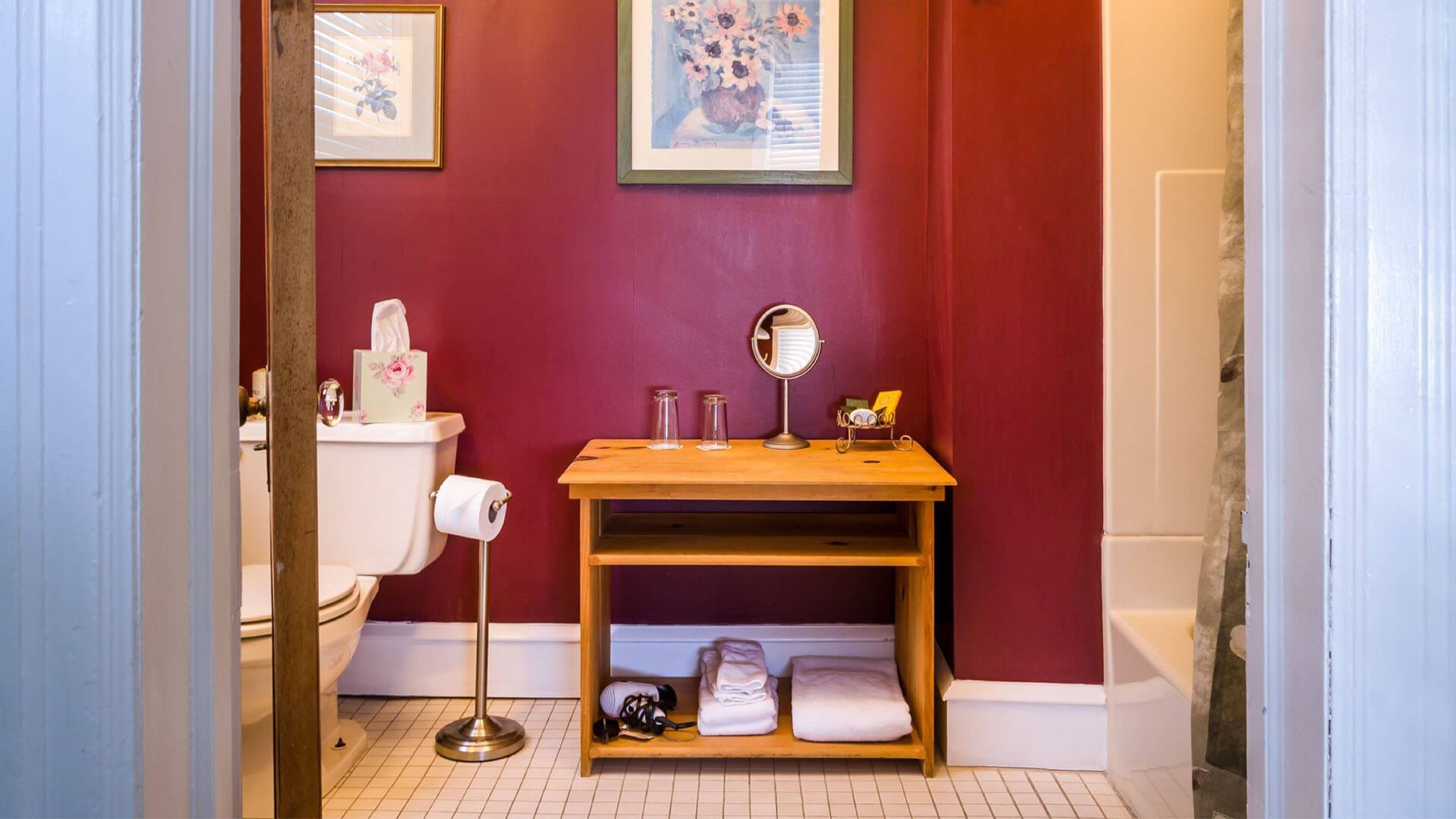 Et badeværelse med toilet, vask, spejl og en hylde med håndklæder.
