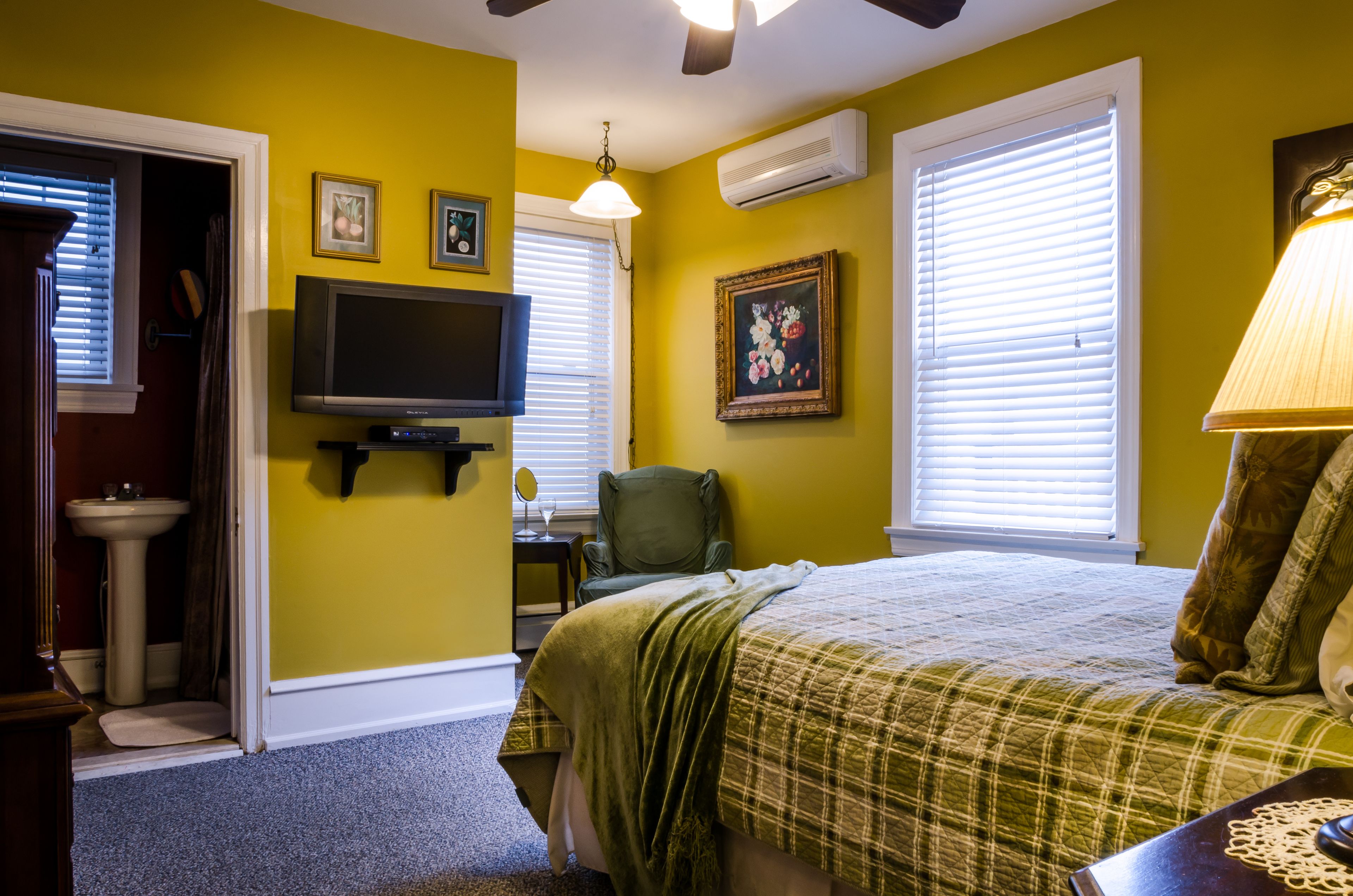 A bedroom with a bed, a television, a chair, and a window with blinds.