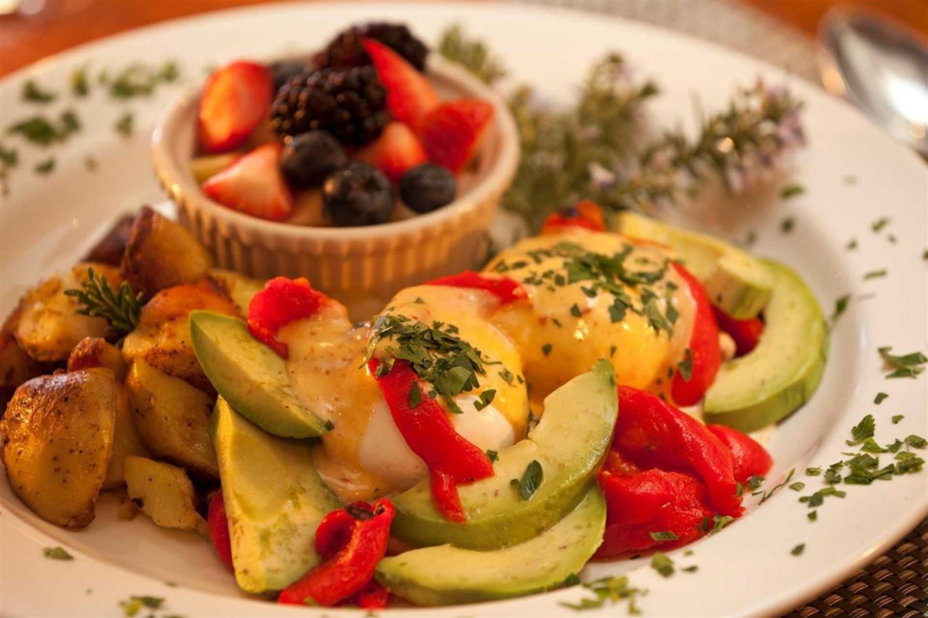 Un plato con huevos pochados, rebanadas de aguacate y pimientos rojos, adornado con hierbas.