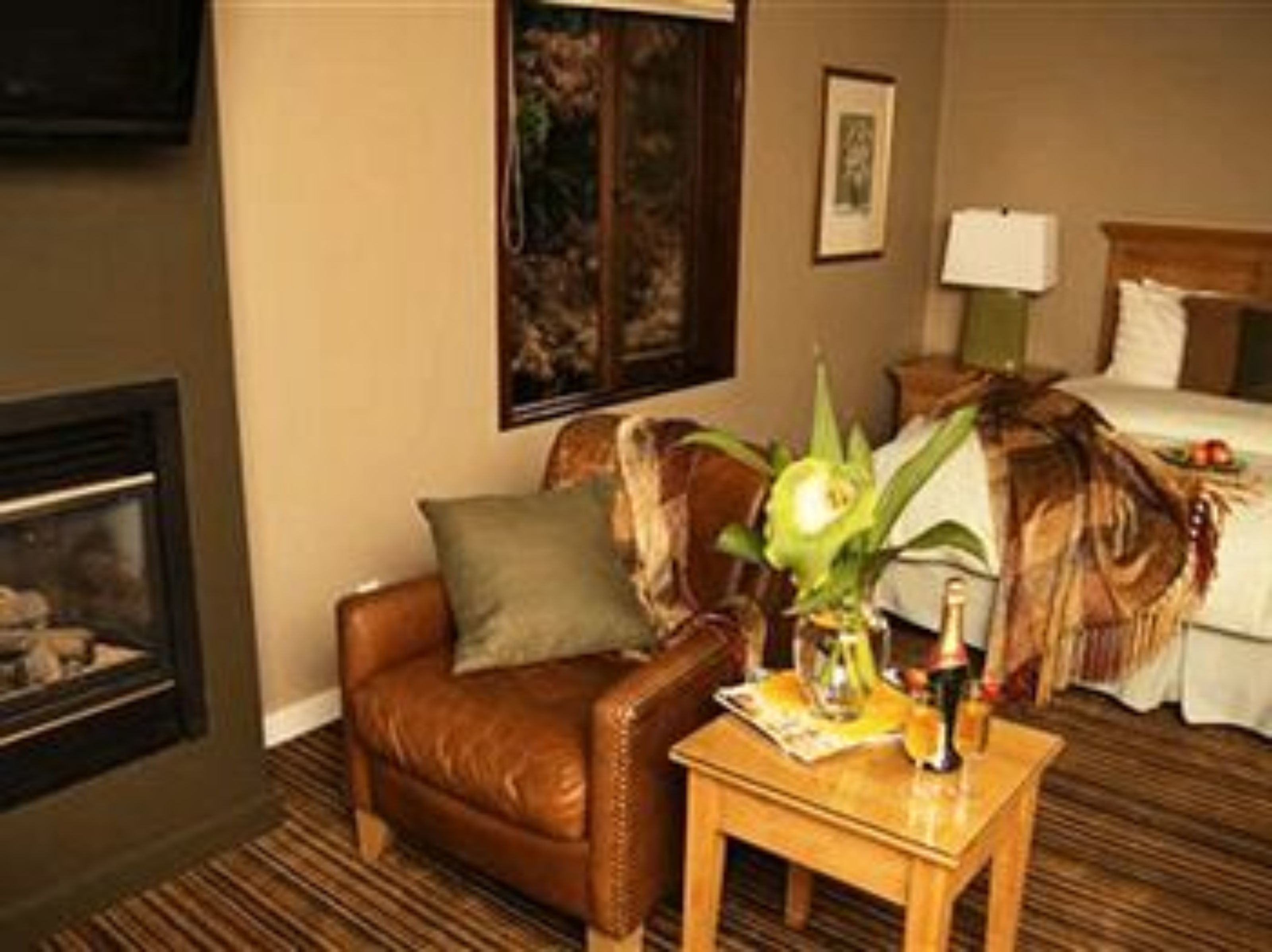 Habitación de hotel con un sillón de cuero, una pequeña mesa de madera, una cama con colcha blanca, un cuadro en la pared y una chimenea.