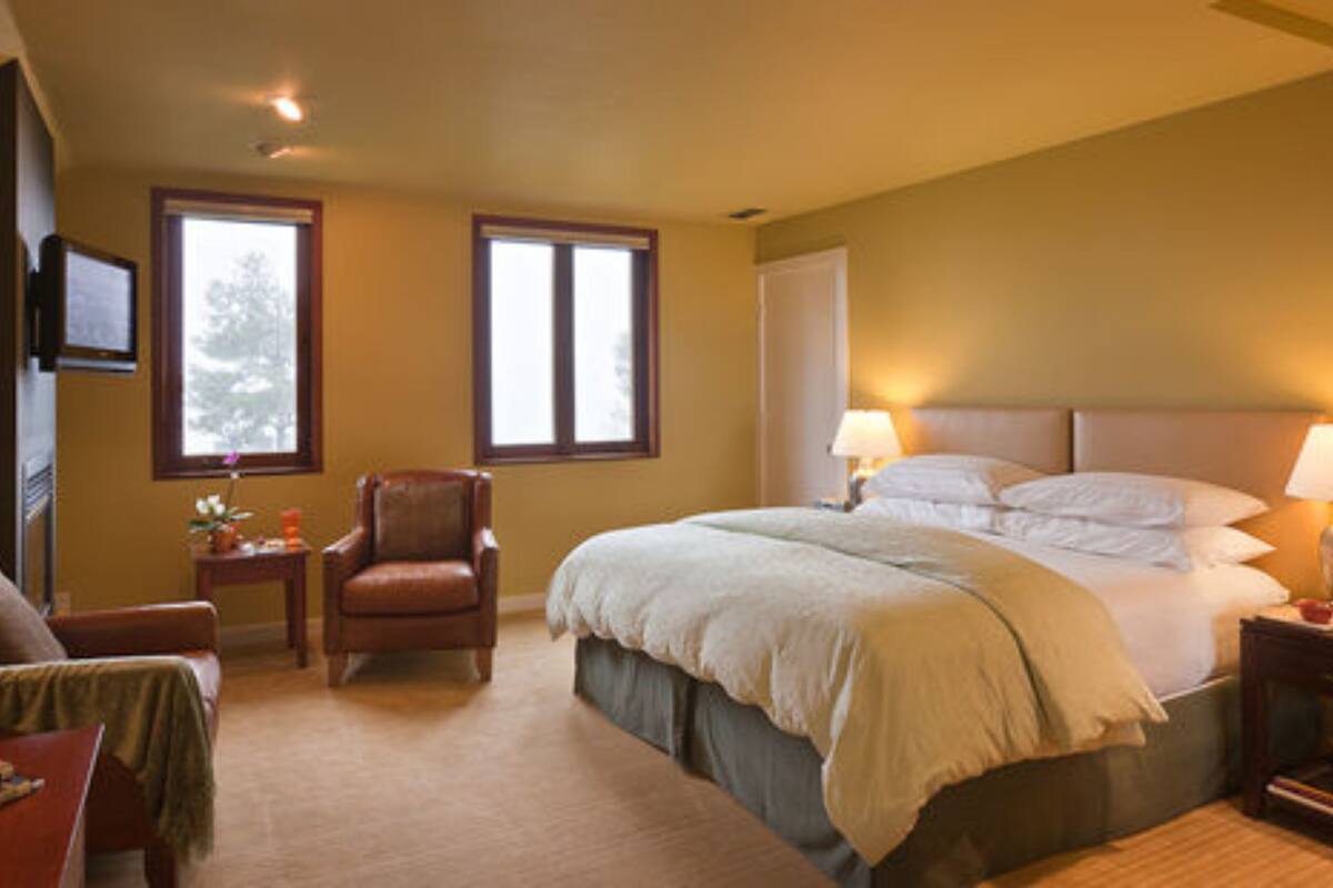 A bedroom with a bed, a chair, a nightstand, a lamp, and a TV on the wall.