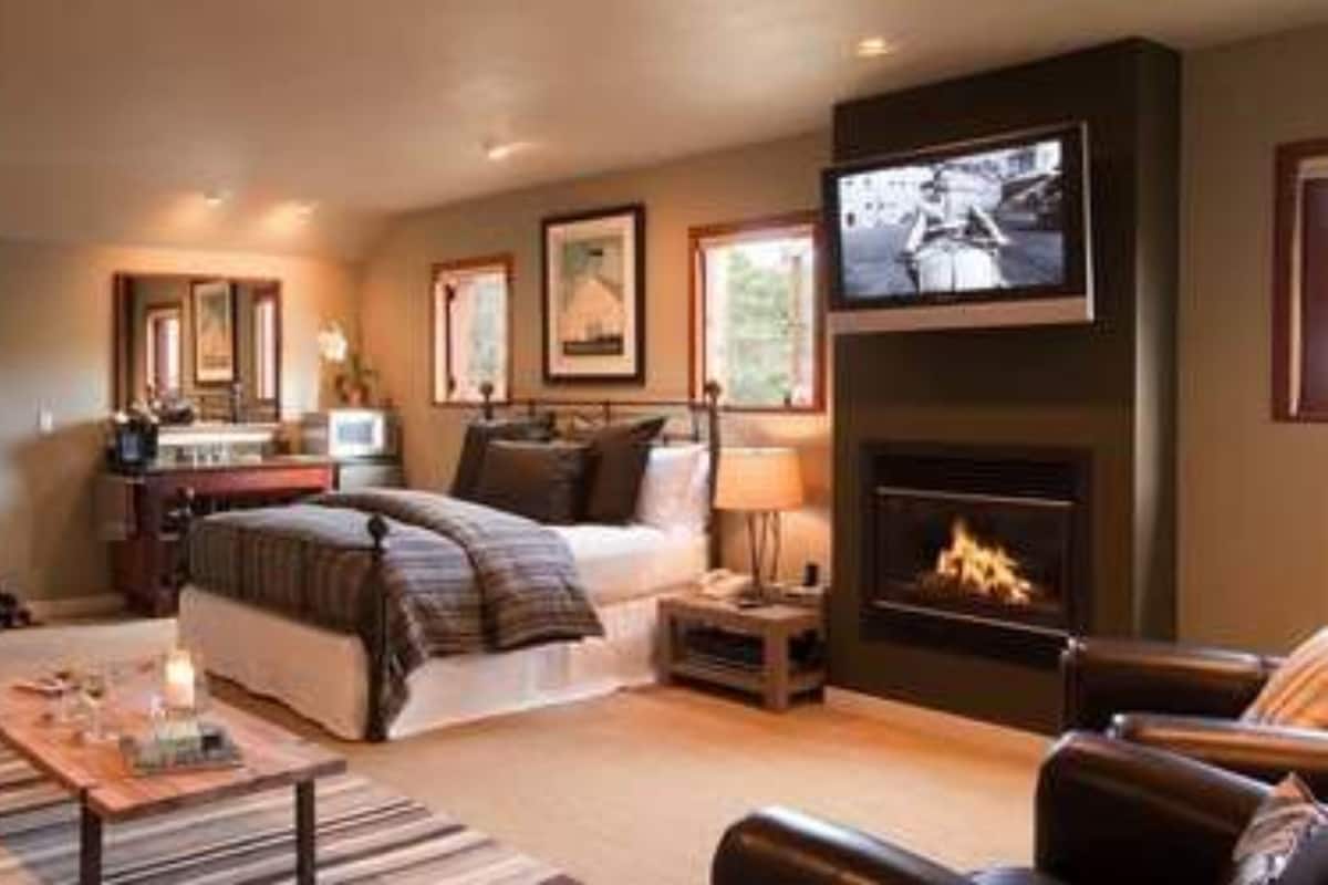 A modern hotel room with a bed, a TV, a fireplace, and a desk with a computer.