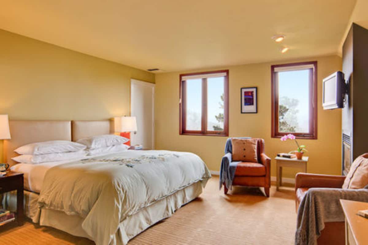 A hotel room with a large bed, two bedside lamps, a chair, a small table, and a TV on the wall.