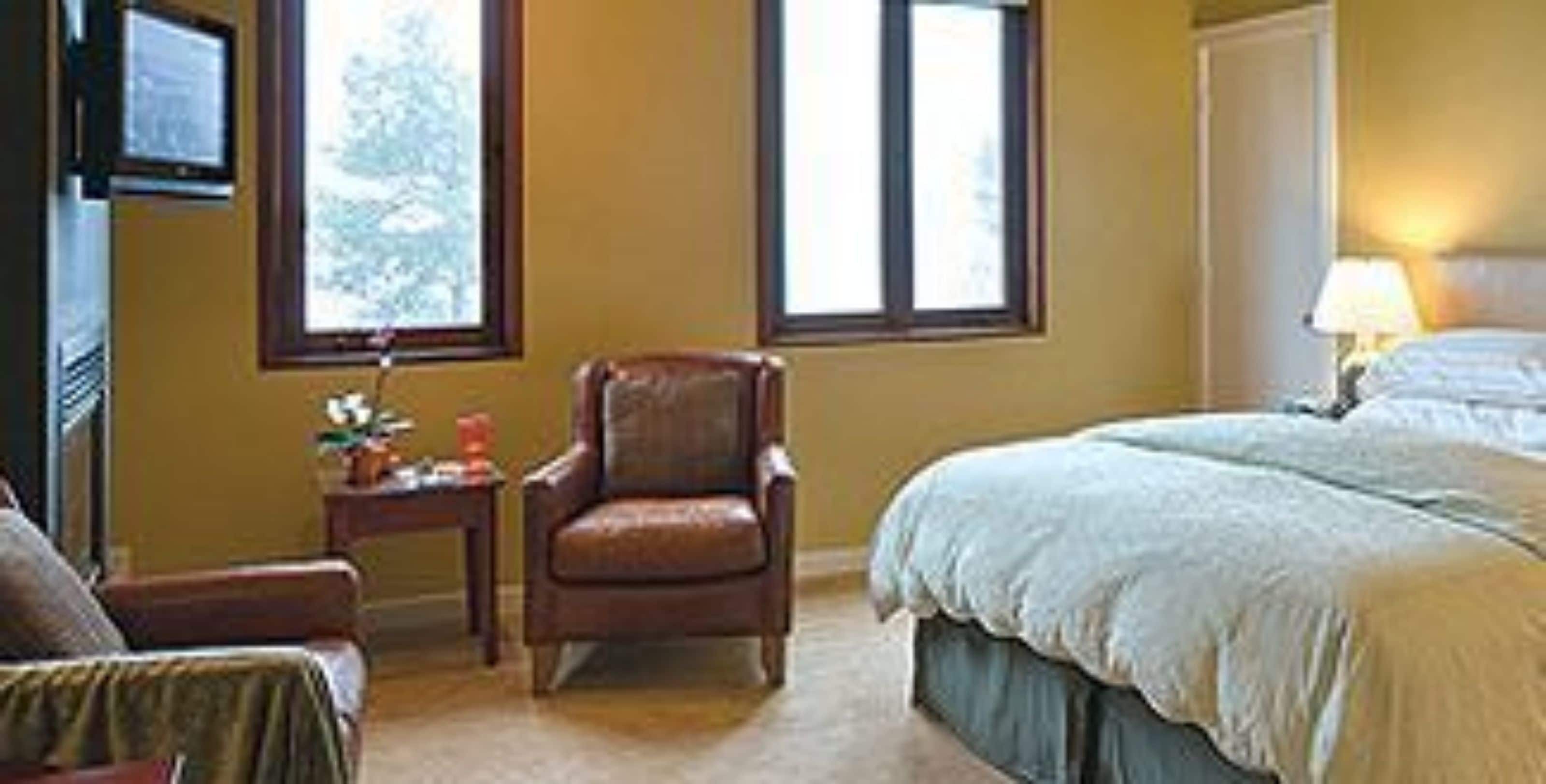 A hotel room with a bed, a chair, a small table, and a window.