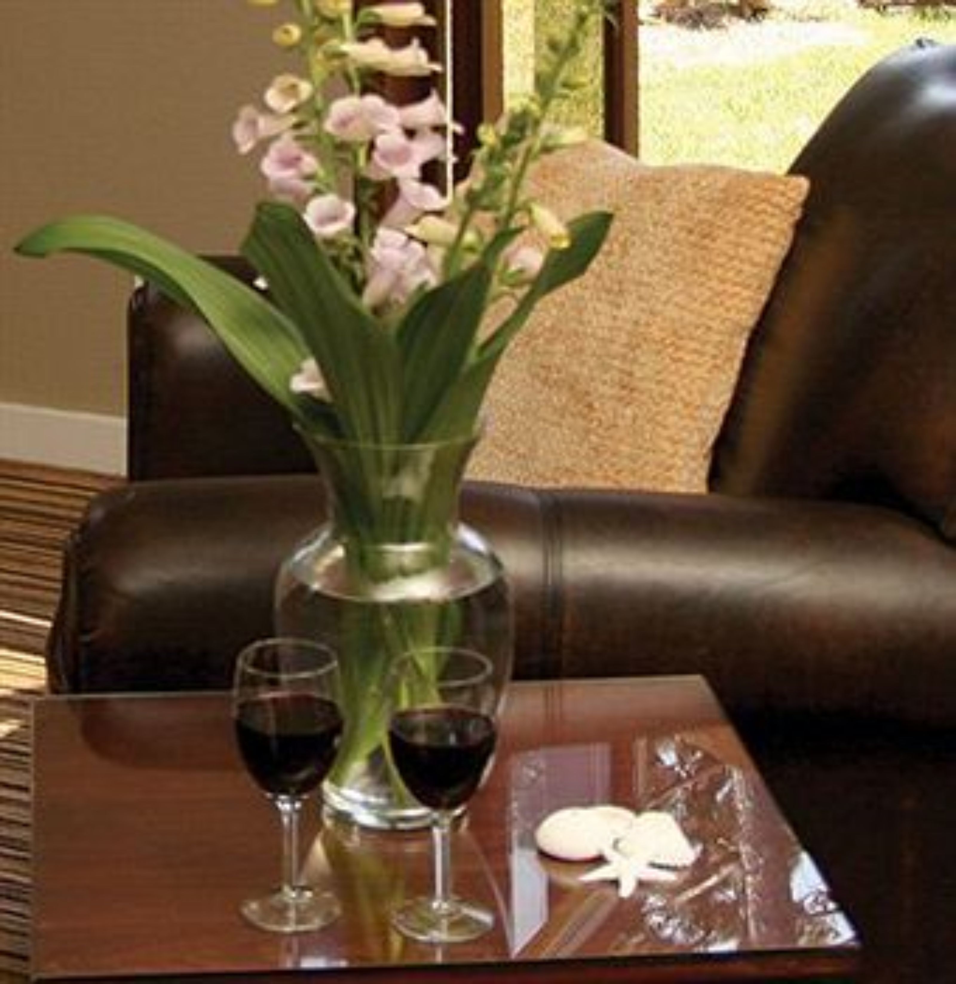 A living room with a brown leather sofa, a glass vase with flowers, and two wine glasses on a wooden table.