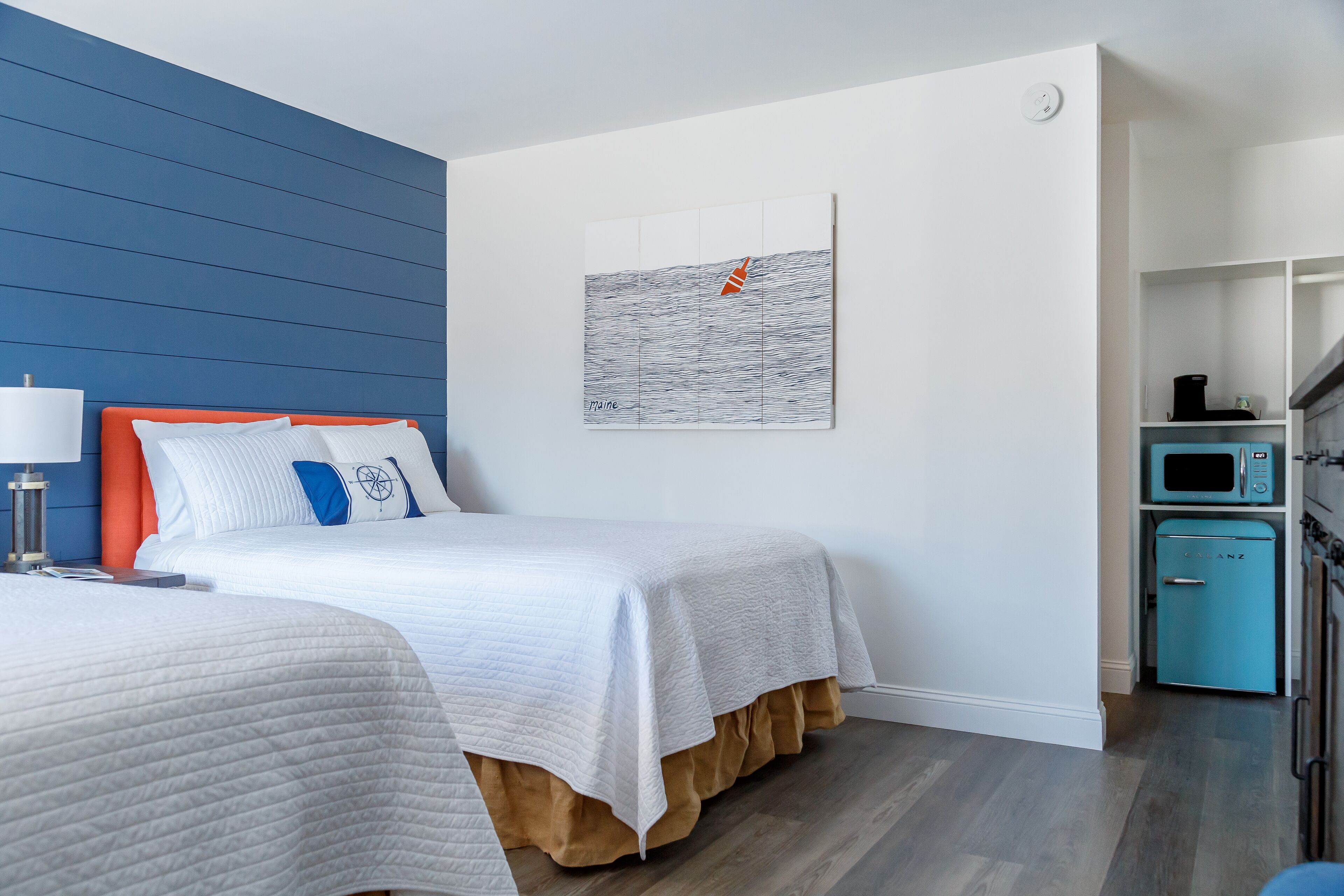 A modern hotel room with a bed, bedside table, and a microwave in the corner.