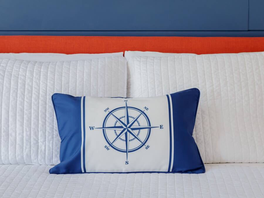 A bed with a quilted white mattress, a blue and white pillow with a compass design, and an orange headboard.