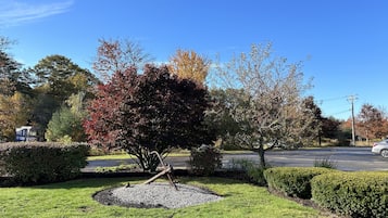 Un jardín bien cuidado con un área central de grava, rodeado de césped y setos podados, bajo un cielo azul despejado.