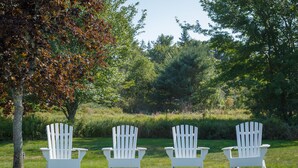 Three white Adirondack chairs in a grassy field with trees in the background. - Flagship Inn and Suites (Boothbay Harbor)