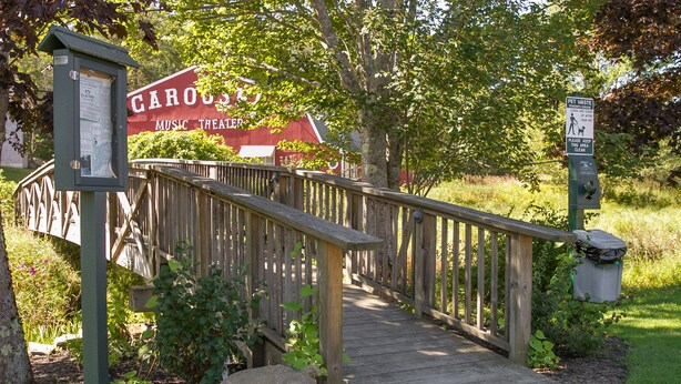 A wooden bridge leading to a building with a sign that reads "CAROUSEL MUSIC THEATER". - Flagship Inn and Suites (Boothbay Harbor)