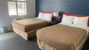 Quarto de hotel com duas camas, uma janela e uma parede azul.