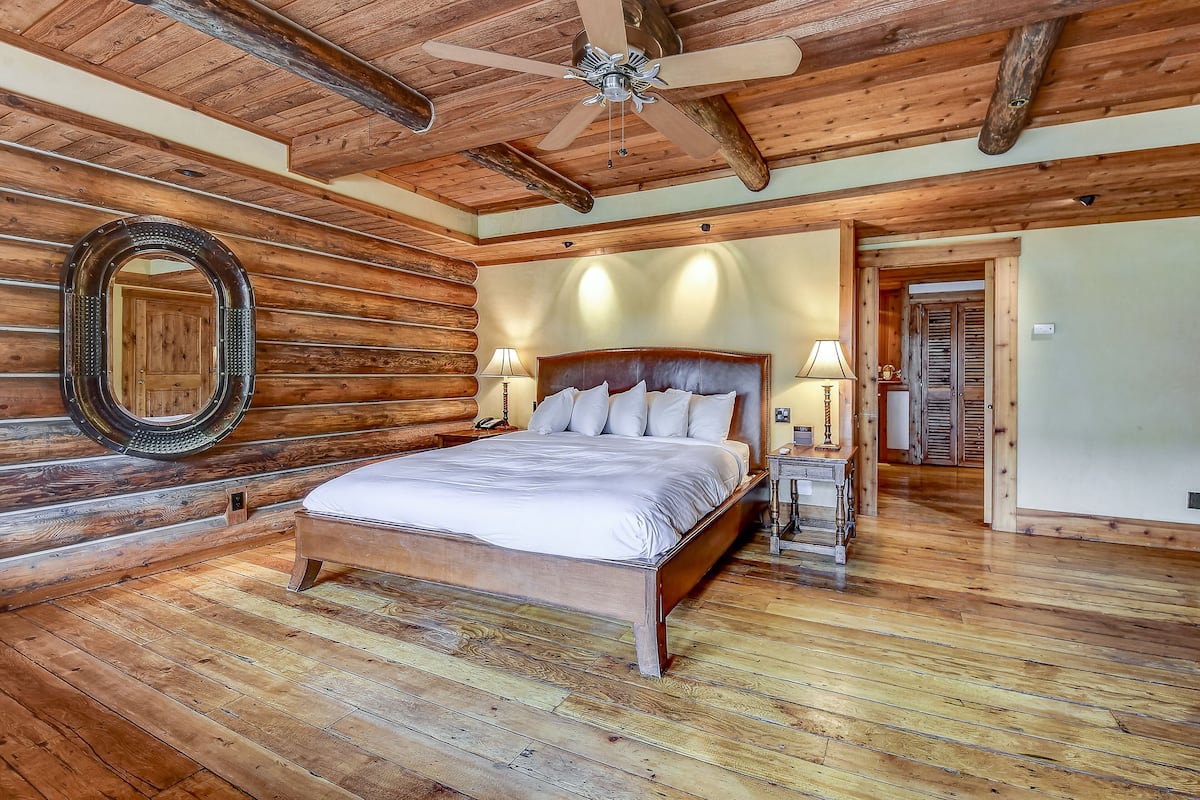 A wooden-paneled bedroom with a large bed, two bedside tables, and a ceiling fan.