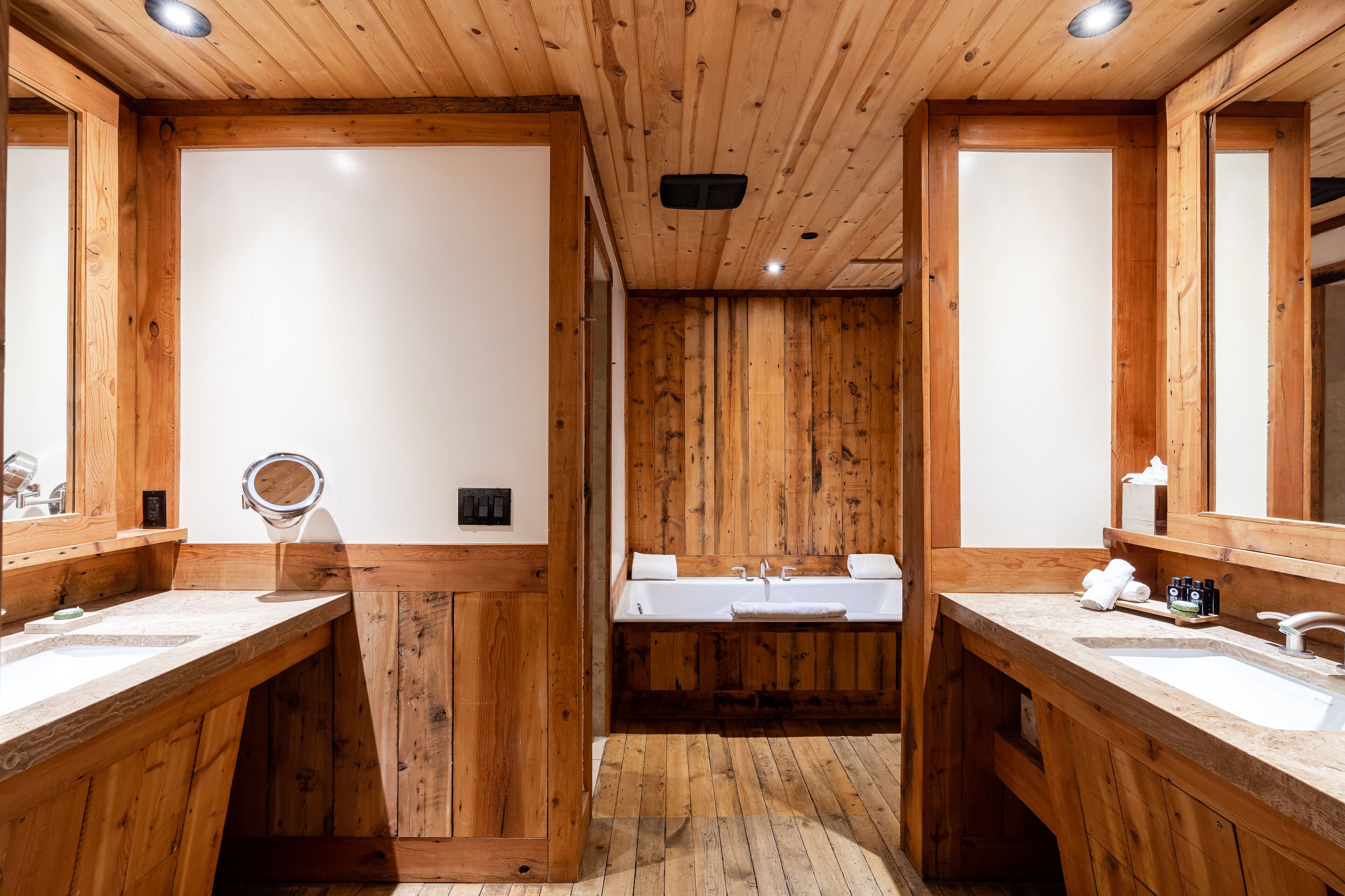 A wooden cabin-style bathroom with two sinks, a mirror, and a shower area.