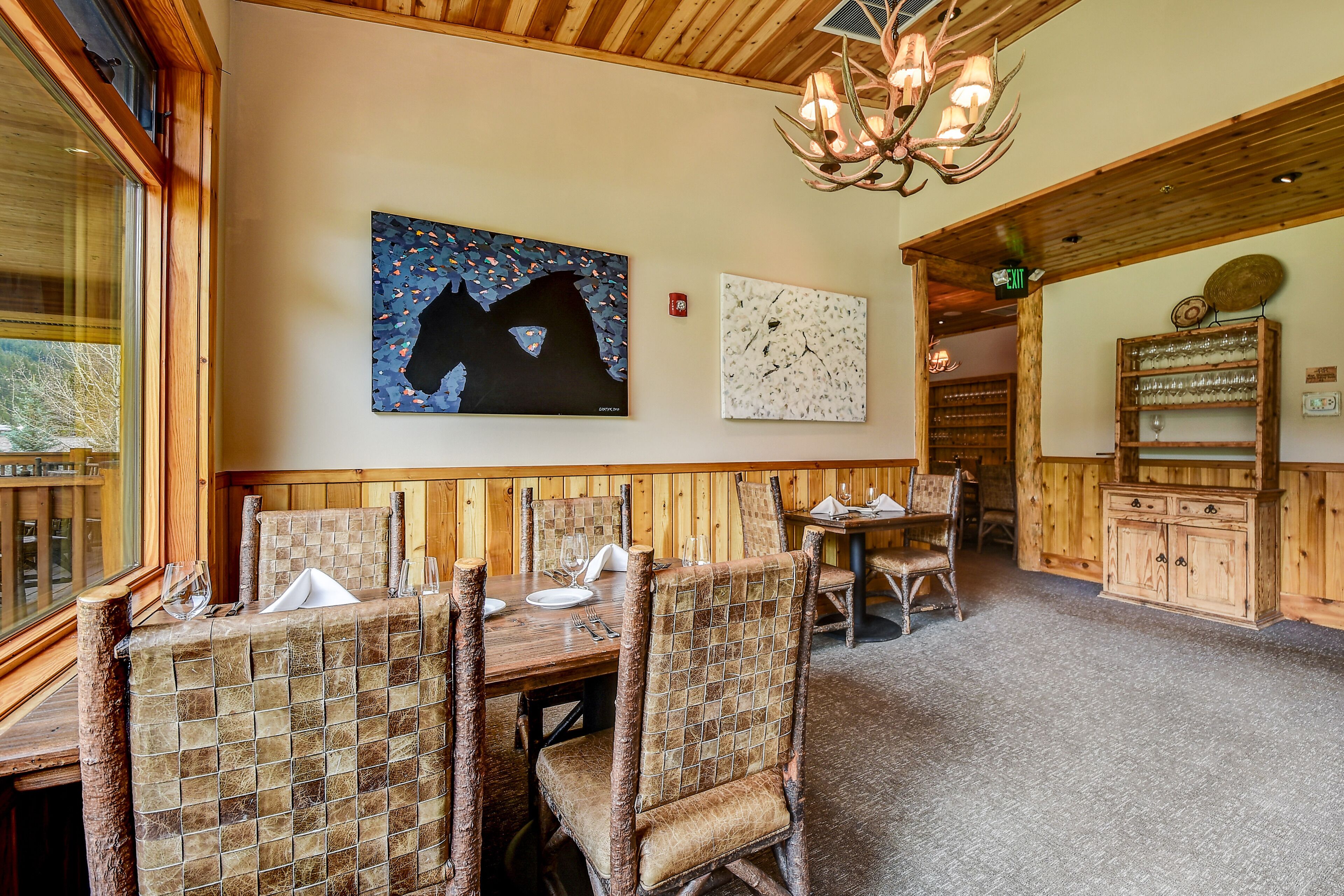 A restaurant with wooden walls and a high ceiling. There are tables and chairs, and a chandelier hangs from the ceiling.