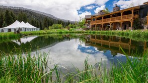 A lakeside lodge with a reflection in the water, a wooden deck, and a mountain backdrop. - Rainbow Ranch Lodge (Gallatin Gateway)