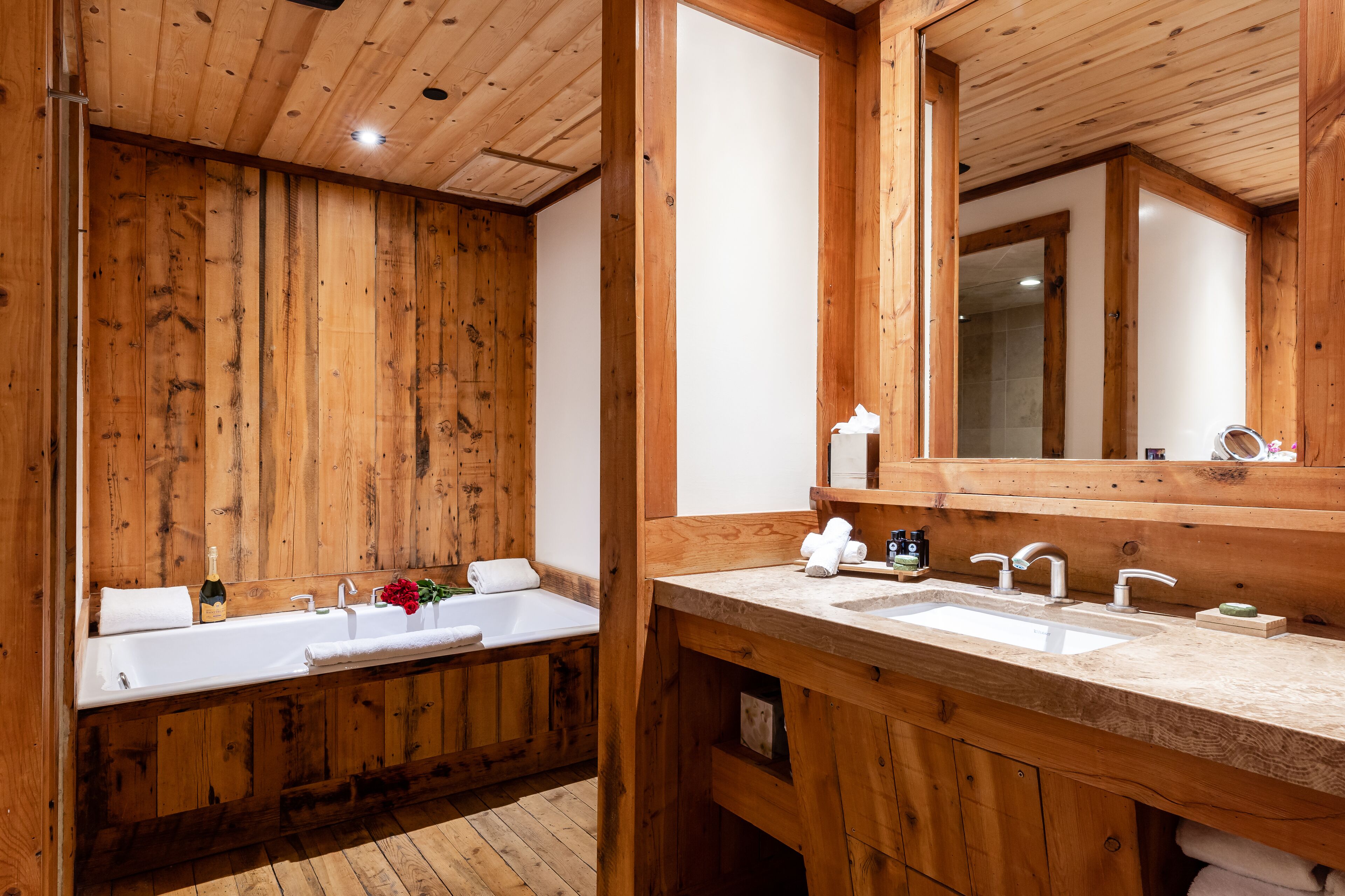 A wooden cabin bathroom with a large wooden wall, a bathtub, a double sink, and a mirror.