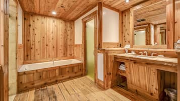 Un baño estilo cabaña de madera con una bañera grande, un tocador con espejo y una zona de ducha.