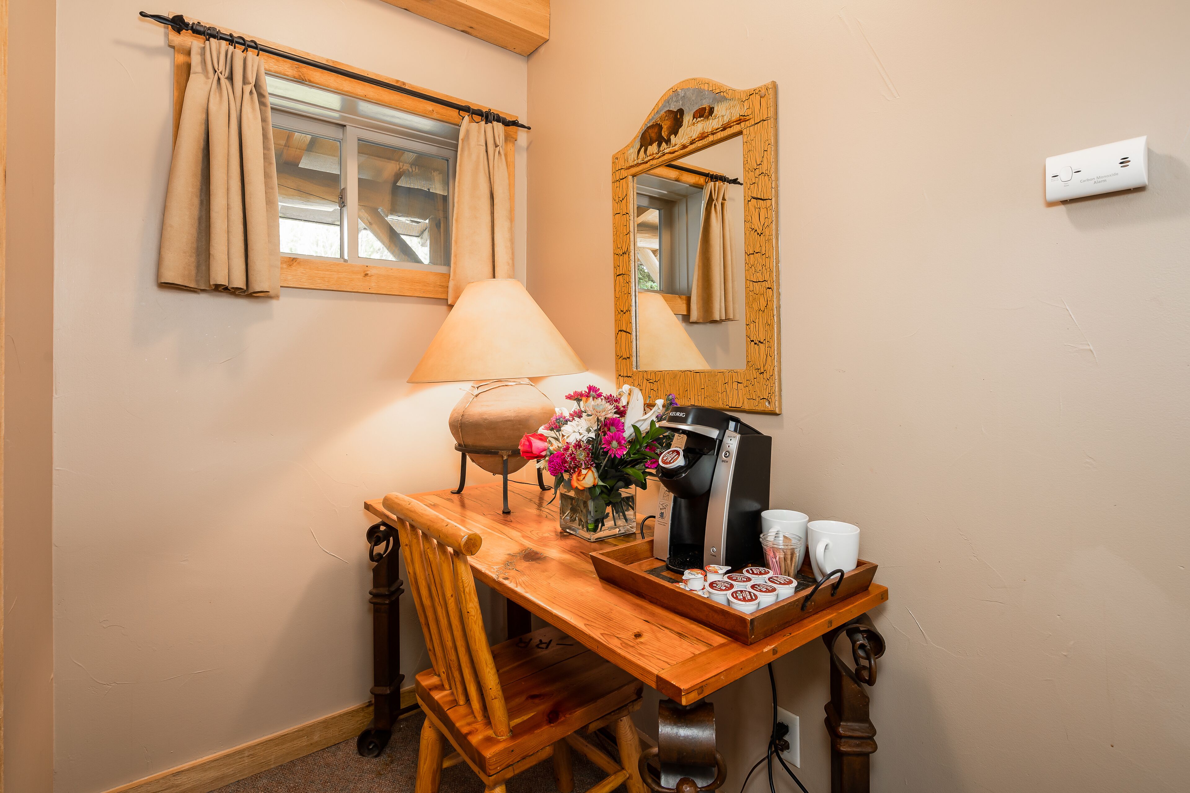 A wooden desk with a coffee maker, cups, and a vase of flowers.