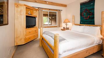 A wooden bed with white linens, a wooden nightstand with a lamp, a wooden wardrobe, and a window with curtains.