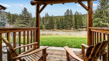 Relax on the deck with Adirondack chairs, surrounded by a lush lawn and evergreen trees.