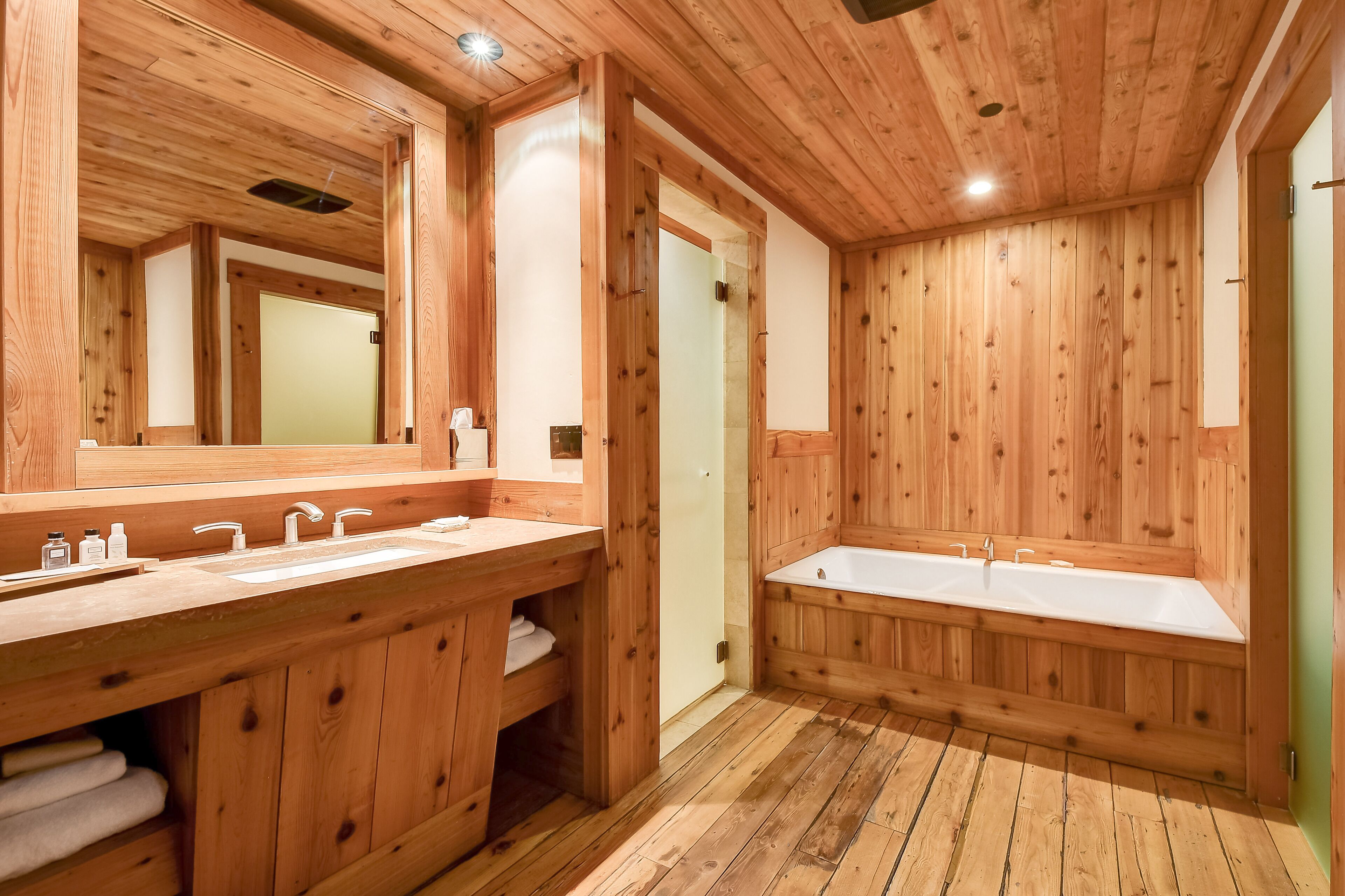 A wooden bathroom with two sinks, a large mirror, and a walk-in shower.