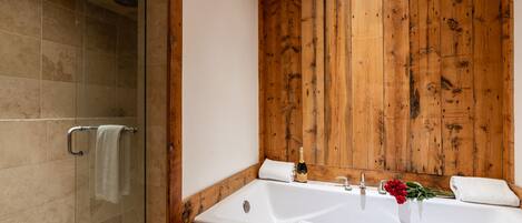A bathroom with a glass shower enclosure, a wooden wall, a large bathtub with a faucet, and a bottle of champagne.