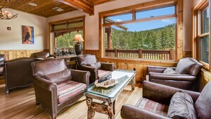 A cozy room with leather chairs, a glass coffee table, and a view of a forest through large windows. - Rainbow Ranch Lodge (Gallatin Gateway)