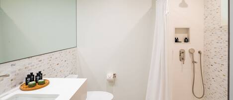 Een badkamer met een wit toilet, een douche met handdouche, een wastafel met toiletartikelen en een spiegel.