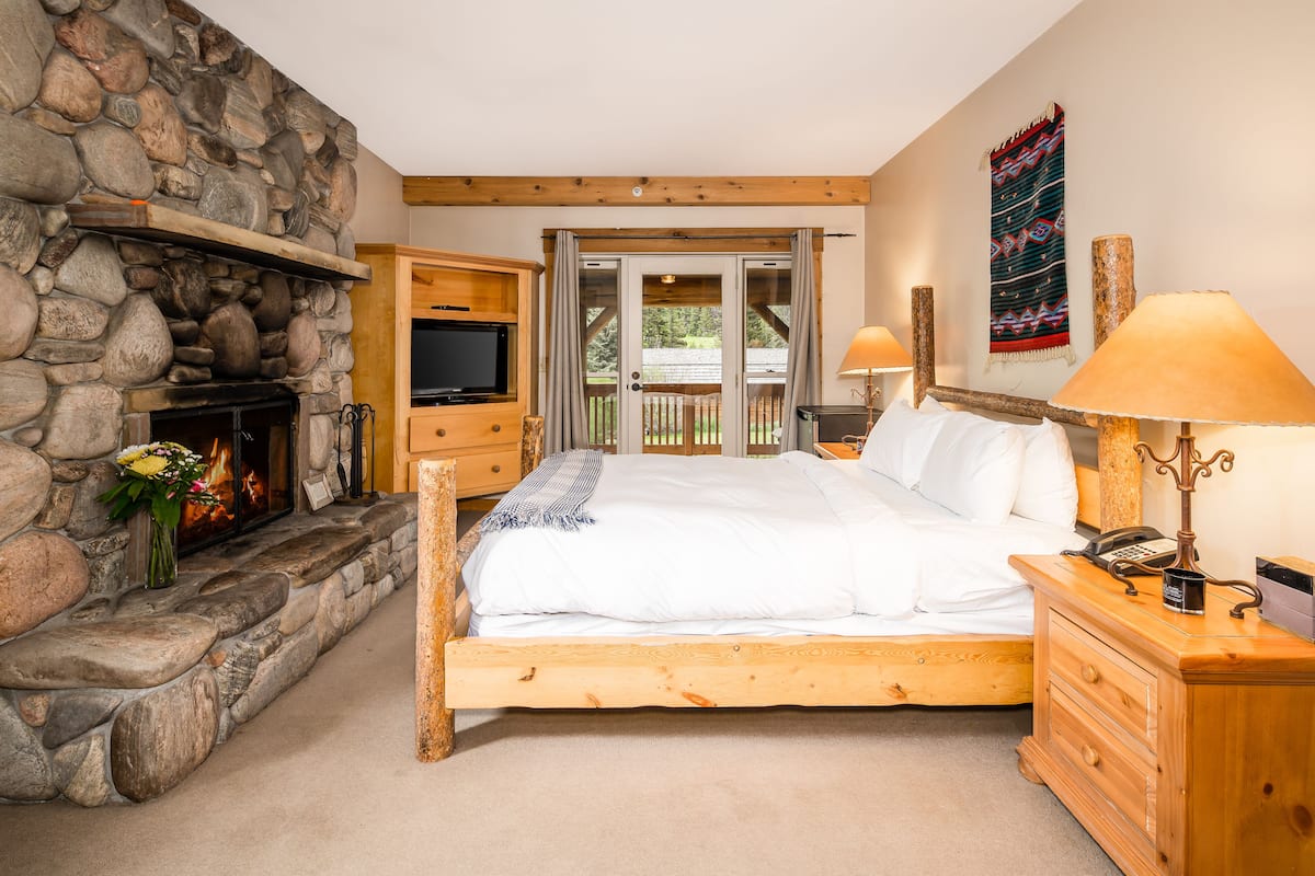 A bedroom with a stone fireplace, wooden bed, and a view of the outdoors through a sliding door.