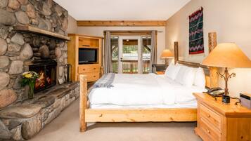 A bedroom with a stone fireplace, wooden bed, and a view of the outdoors through a sliding door.