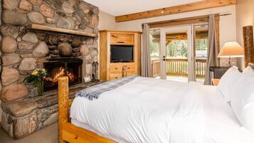 A bedroom with a stone fireplace, a television, and a balcony with a wooden deck.