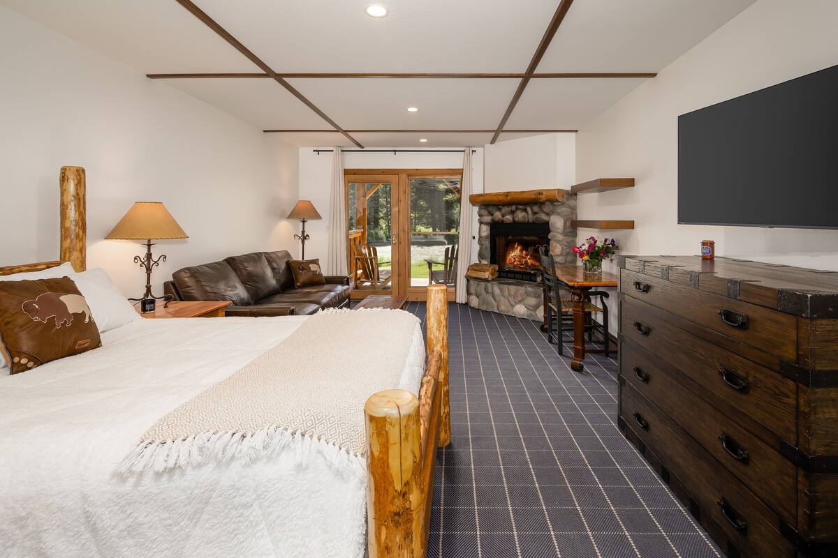 A bedroom with a large bed, a stone fireplace, a wooden dresser, and a television.