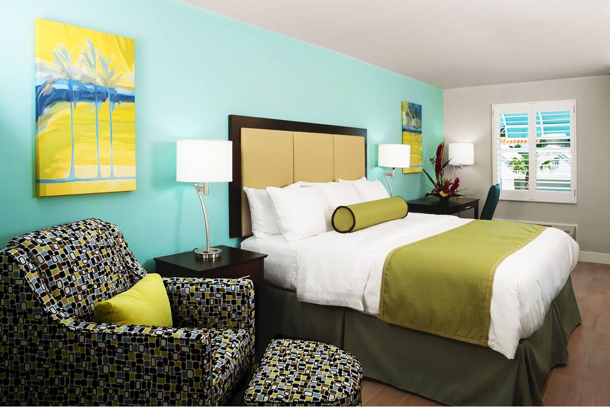 A hotel room with a bed, two chairs, a nightstand, and artwork on the walls.
