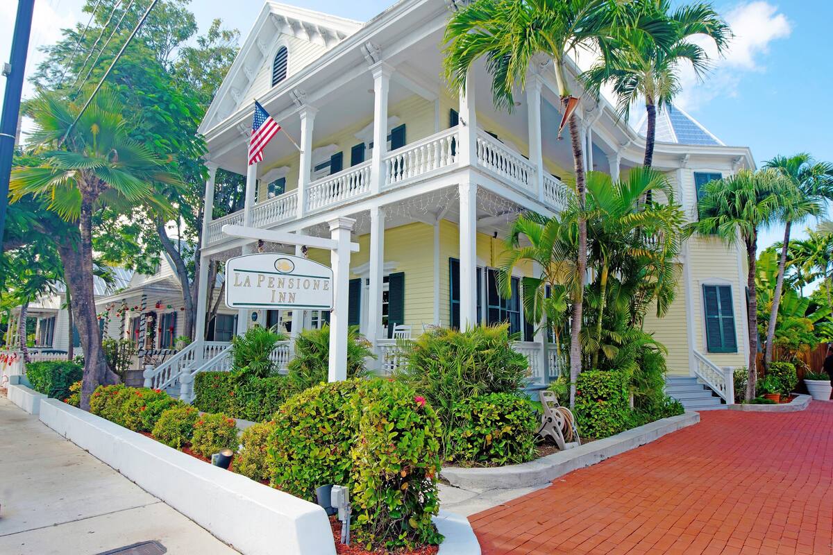 A two-story hotel with a balcony, surrounded by lush greenery and palm trees.