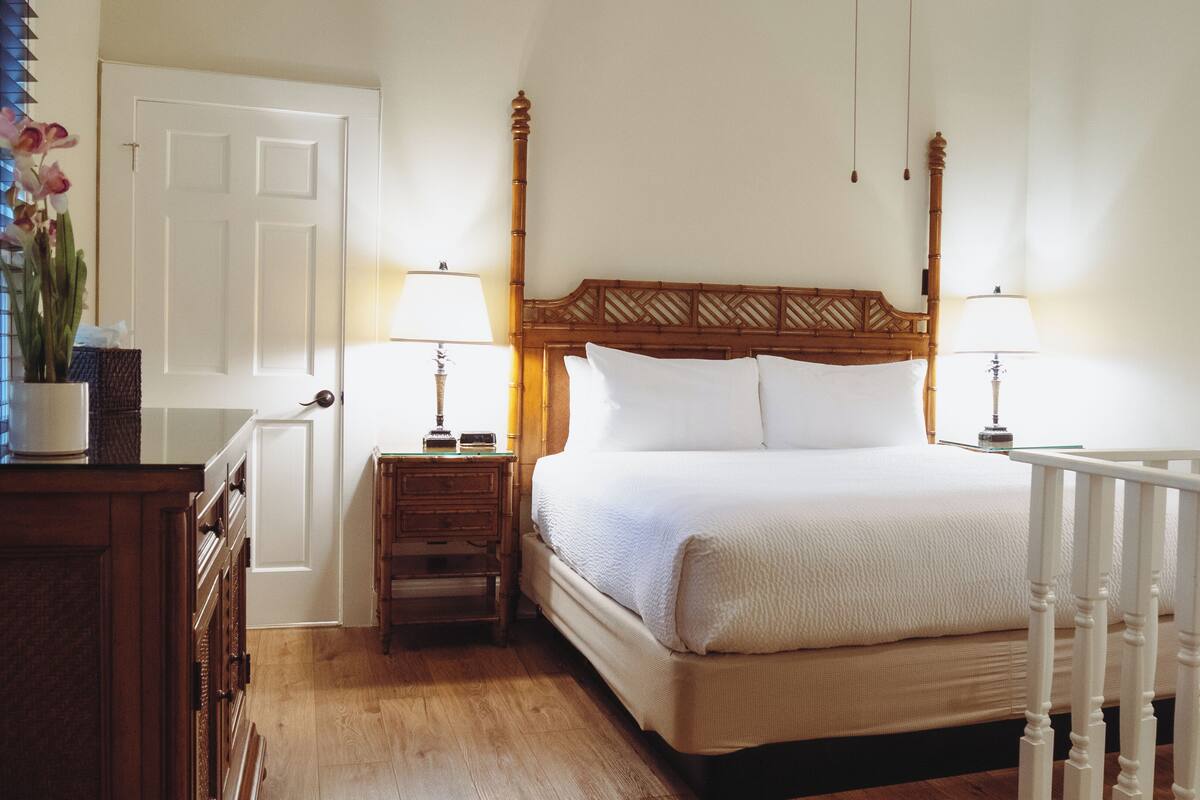 A neatly arranged bedroom with a wooden headboard, two bedside tables with lamps, a white door, and a white railing.