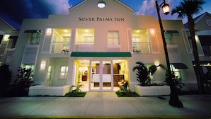 The exterior of the Silver Palms Inn with a two-story structure, a green awning over the entrance, and a palm tree to the right.