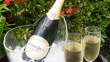 Una botella de champán Perrier Jouët en un balde con hielo, dos copas de champán llenas, y un fondo de follaje verde y flores rojas.
